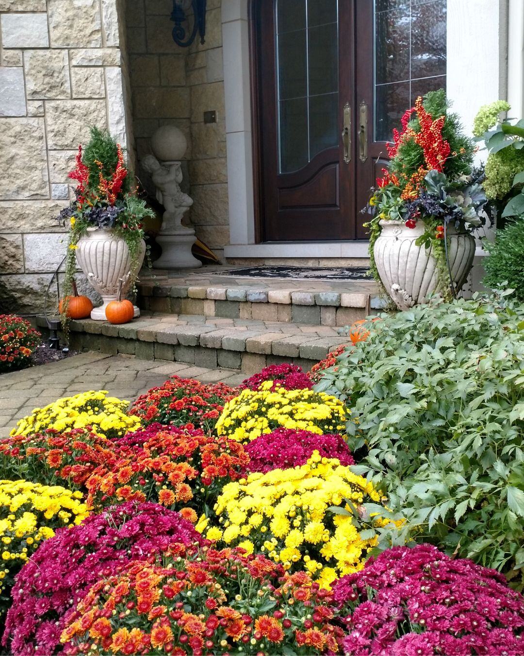 Front entry steps lined with mounded red, yellow and pink mums and urns of fall plantings.