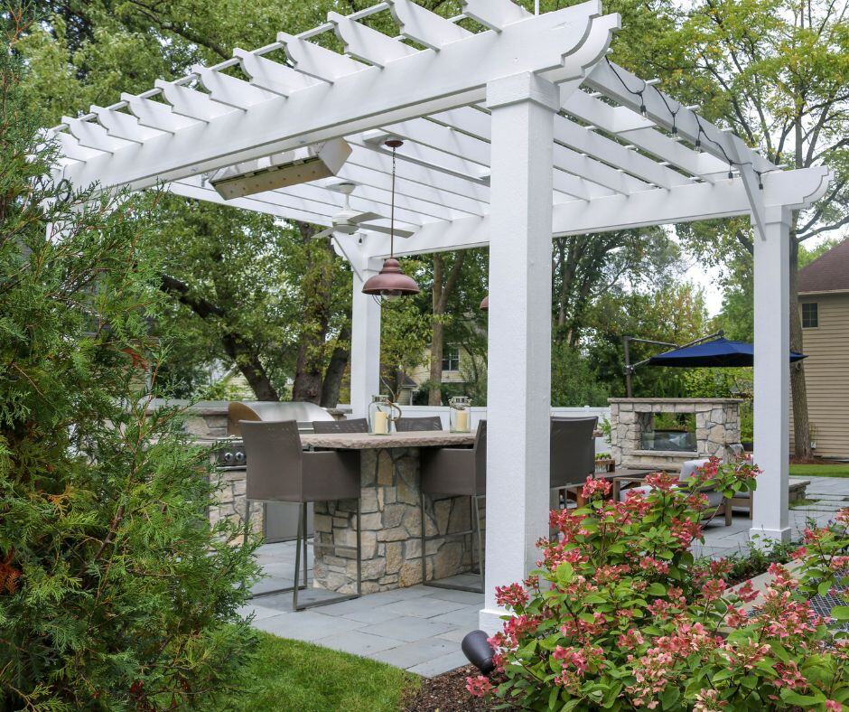 White pergola over an outdoor kitchen and seating area framed by hydrangeas.